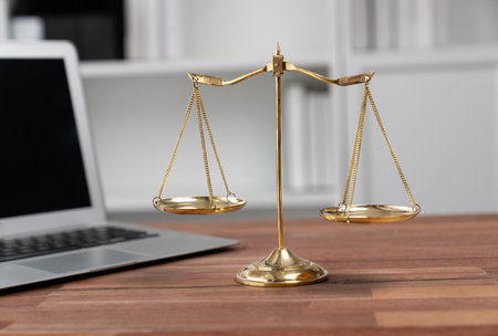 Symbolizing justice and legal authority, golden balanced scale on desk with laptop in law office background, reflecting concept of equality and fair judgment by lawyer and judge. equilityの写真素材