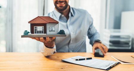 Focus house sample model held by blurred smiling and happy real estate agent or buyer in office in front of the camera. Ferventの写真素材