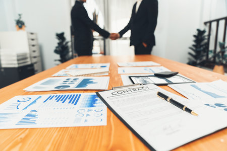Closeup professional businessman shaking hands over desk in modern office after successfully analyzing pile of dashboard data paper as teamwork and integrity handshake in workplace concept. ferventの写真素材