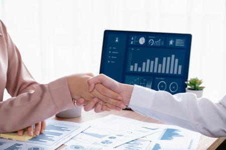 Closeup businesswomen shaking hand in modern office after successfully analyzing piles of dashboard data papers, as importance of teamwork and integrity in the workplace concept. Enthusiasticの写真素材