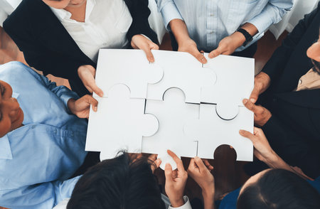 Diverse corporate officer workers collaborate in office, connecting puzzle pieces to represent partnership and teamwork. Unity and synergy in business concept by merging jigsaw puzzle. Concordの写真素材