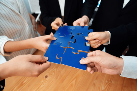 Closeup top view business team of office worker putting jigsaw puzzle together over table filled with financial report paper in workplace with manager to promote harmony concept in meeting room.の写真素材