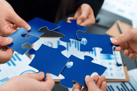Closeup top view business team of office worker putting jigsaw puzzle together over table filled...