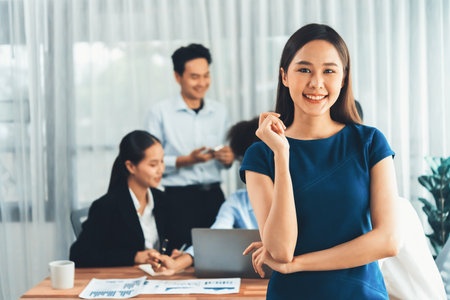 Young Asian businesswoman poses confidently with diverse coworkers in busy meeting room background. Multicultural team works together for business success. Office lady portrait. Concordの写真素材