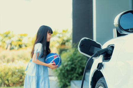 Focus home electric charging station for electric vehicle as alternative clean sustainable energy technology concept with blurred progressive young girl playing in the background at her home.の写真素材