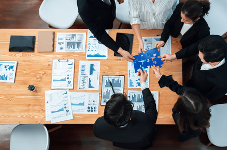 Top view businesspeople and colleagues in formal wear putting jigsaw puzzles together over meeting table with financial report papers in harmony office for team building concept.の写真素材