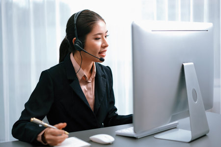 Asian call center with headset and microphone working on her laptop. Female operator provide exceptional customer service. Supportive call center agent helping customer on inquiry. Enthusiasticの写真素材