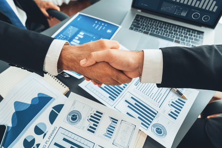 Closeup professional businessman shaking hands over desk in modern office after successfully analyzing pile of dashboard data paper as teamwork and integrity handshake in workplace concept. ferventの写真素材