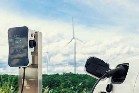 Progressive combination of wind turbine and EV car, future energy infrastructure. Electric vehicle being charged at charging station powered by renewable energy from wind turbine in the countryside.の写真素材