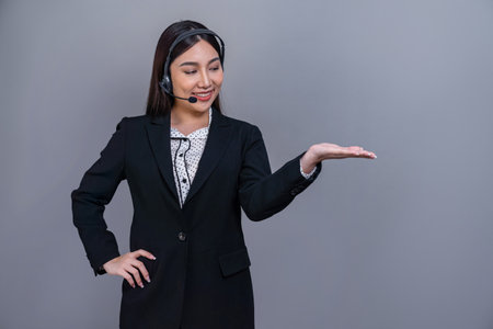 Female call center operator wearing headset and formal suit standing confidently with holding hand gesture for product advertisement or HR recruitment on isolated background. Jubilantの写真素材