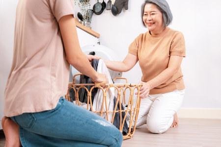 Daughter and mother working together to complete their household chores near the washing machine in a happy and contented manner. Mother and daughter doing the usual tasks in the house.の写真素材