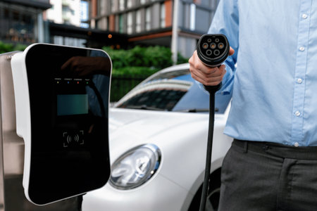 Closeup progressive hand holding EV charger plug and pointing at camera with his electric car...