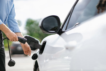Closeup progressive man holding EV charger plug from public charging station for electric vehicle...