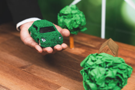 Businessman holding green eco car model in office. Electric vehicle utilized by eco-friendly business for environmental friendly transportation. Corporate responsible with zero CO2 emission. Alterの写真素材