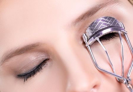 Closeup alluring facial makeup, beautiful woman with perfect smooth cosmetic clean skin correct eyelash curler with metal mechanic beauty accessory in isolated background.の写真素材