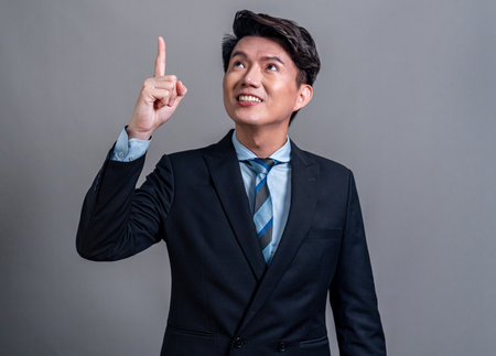 Confident Asian businessman posing in professional outfit on isolated background. Office worker pointing finger gesture for product sales promotions advertisements or HR recruitment image. Jubilantの写真素材