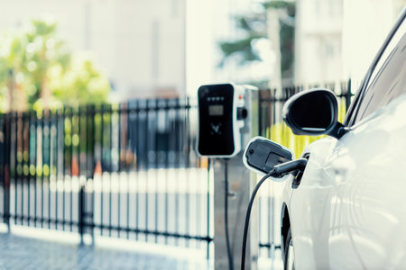 Focus closeup electric vehicle plugged in with EV charger device from blurred background of public charging station powered by renewable clean energy for progressive eco-friendly car concept.の写真素材