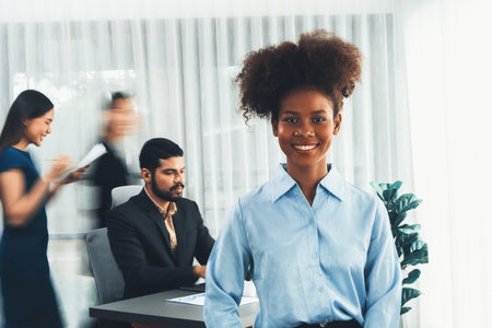 Young African businesswoman portrait poses confidently with diverse coworkers in busy meeting room in motion blurred background. Multicultural team works together for business success. Concordの写真素材
