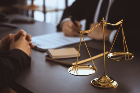 Focus shiny golden balanced scale on blurred background of lawyer colleagues working on desk at law...
