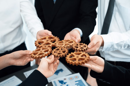 Closeup top view businesspeople hand holding gear and join together over meeting table with financial report papers. Cohesive group of office workers holding cog wheel as synergy harmony concept.の写真素材