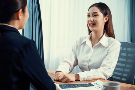 Two asian women conduct job interview in office. Applicants wear formal suit while talking about her CV and job application. Interviewer ask inquiry in positive and conversational manner. Enthusiasticの写真素材