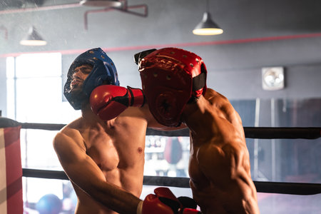 Two athletic and muscular body boxers with safety helmet or boxing head guard face off in fierce boxing match. Boxing fighter competitor fighting in the boxing ring. Impetusの写真素材