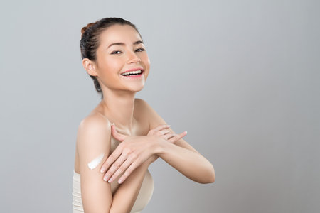 Glamorous beautiful woman applying moisturizer cream on her arm for perfect skincare treatment in isolated background. Soft makeup young girl portrait with skin rejuvenation and cosmetology concept.の写真素材