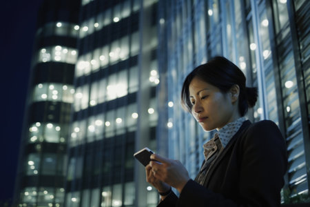 Wide angle shot of a senior chinese japanese businesswoman executive using mobile phone with background of modern office buildings at night. Generative AI AIG18.の素材