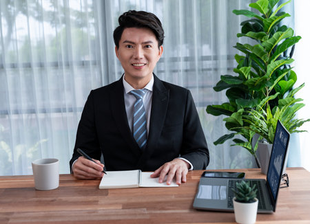 Businessman working on laptop for on office desk workspace portrait. Smart executive researching financial business data or planning strategic business marketing with computer on table. Jubilantの写真素材