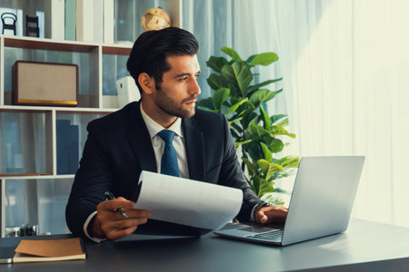 Modern professional businessman at modern office desk using laptop to work and write notes. Diligent...