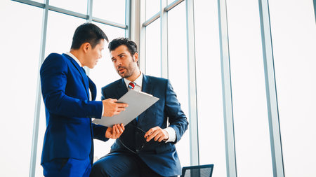 Two business people talk project strategy at office meeting room. Businessman discuss project planning with colleague at modern workplace while having conversation and advice on financial report. Jivyの写真素材