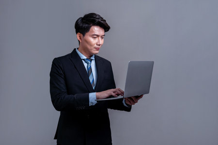 Confident young Asian businessman posing with laptop on isolated background. Office worker make hand holding gesture for innovative product advertisements, promotion sales or HR recruitment. Jubilantの写真素材