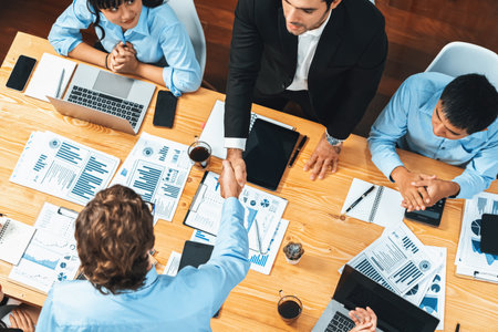Two businessman shake hand in meeting room with coworker give cheerful applause. Team of analyst celebrate after successful significant progress on business strategic performance. Meticulousの写真素材