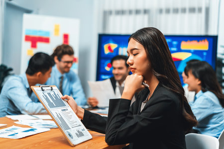 Portrait of happy young asian businesswoman or analyst looking at camera with her colleague analyzing data analysis in dynamic business strategy investment planning meeting. Habilimentの写真素材