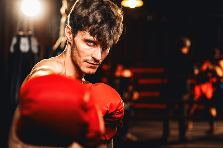 Boxing fighter shirtless posing, caucasian boxer punch his fist in front of camera in aggressive stance and ready to fight at gym with kicking bag and boxing equipment in background. Impetusの写真素材