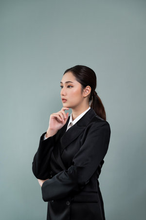 Confident young businesswoman stands on isolated background, posing in formal black suit. Office lady or manager with smart and professional appearance. Enthusiasticの写真素材