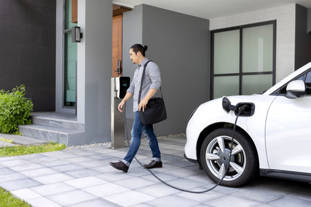 Progressive asian man and electric car with home charging station. Concept of the use of electric vehicles in a progressive lifestyle contributes to a clean and healthy environment.の写真素材