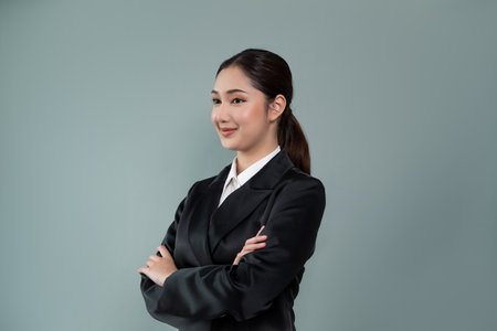 Confident young businesswoman stands on isolated background, posing in formal black suit. Office lady or manager with smart and professional appearance. Enthusiasticの写真素材