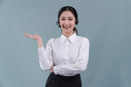 Asian female call center operator with smile face advertises job opportunity, wearing a formal suit and headset holding hand gesture for product on customizable isolated background. Enthusiasticの写真素材