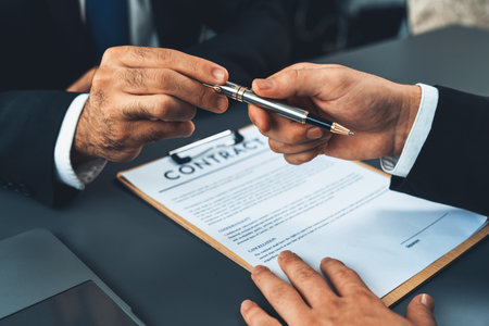Two businesspeople sit across the desk as business deal is taking place. Corporate attorney giving a pen for client or partner to sign contract paper, sealing the deal with signature. Ferventの写真素材