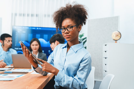 Happy young african businesswoman wearing glasses portrait with group of office worker on meeting with screen display business dashboard in background. Confident office lady at team meeting. Concordの写真素材