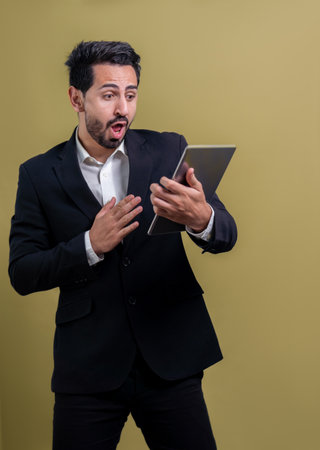 Confident businessman in formal suit holding tablet with surprise look for promotion or advertising. Facial expression and gestures indicate excitement and amazement on an isolated background. Ferventの写真素材