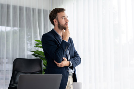 Handsome businessman in black suit stand confidently in his modern office portrait, deep in thought about business with pensive gazing expression, thinking strategically about his next move. Entityの写真素材