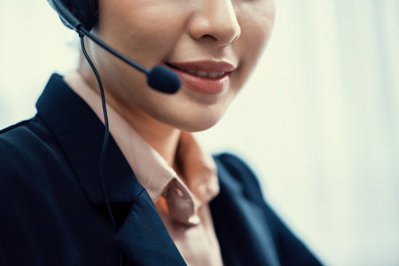 Asian call center with headset and microphone working on her workspace looking at camera. Female operator provide exceptional customer service. Supportive call center agent portrait. Enthusiasticの写真素材