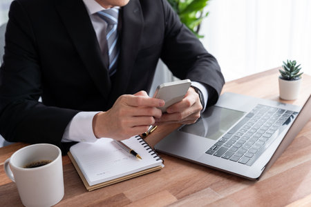Businessman working on laptop for on office desk workspace with his smartphone. Smart executive researching financial business data or planning strategic business, talking on phone. Jubilantの写真素材
