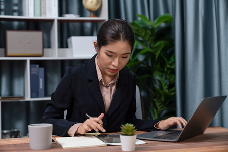 Young asian businesswoman is diligently working and taking notes in her modern office workspace, demonstrating professionalism as attractive and diligent office lady. Enthusiasticの写真素材