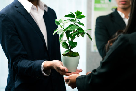 Eco-friendly investment on reforestation by group of business people holding plant together in office promoting CO2 reduction and natural preservation to save Earth with sustainable future. Quaintの写真素材