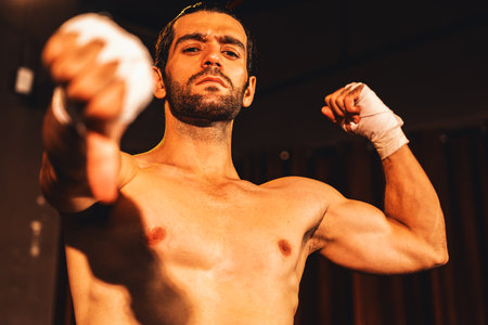 Boxing fighter shirtless posing, caucasian boxer punch his bare fist and wrap in front of camera, aggressive stance and ready to fight at the boxing ring. Impetusの写真素材
