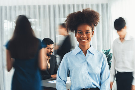 Young African businesswoman portrait poses confidently with diverse coworkers in busy meeting room in motion blurred background. Multicultural team works together for business success. Concordの写真素材