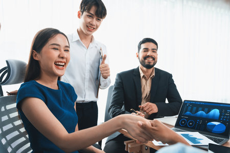 Diverse coworkers celebrate success with handshake and teamwork in corporate workplace....